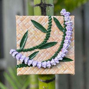 May include: A purple and green lei made of fabric flowers on a woven background.