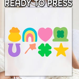 May include: A white t-shirt with a design of various lucky charms, including a pot of gold, a rainbow, a heart, a four-leaf clover, a horseshoe, a star, and a leprechaun hat. The text "READY TO PRESS" is at the top of the shirt.