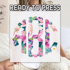 May include: A square canvas featuring a floral monogram design. The letters, in a stylized font, are filled with a vibrant pattern of pink, purple, and blue flowers. The text "READY TO PRESS" is displayed at the top.