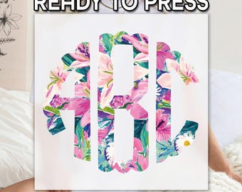 May include: A square canvas featuring a floral monogram design. The letters, in a stylized font, are filled with a vibrant pattern of pink, purple, and blue flowers. The text "READY TO PRESS" is displayed at the top.