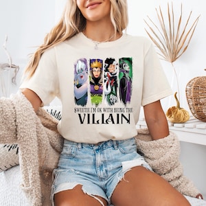 Puede incluir: Camiseta color crema con un dise&ntilde;o de cuatro villanos de dibujos animados: &Uacute;rsula, la Reina Malvada, Cruella de Vil y Mal&eacute;fica. El texto en la camiseta dice: "Sweetie I'm OK with being the Villain".