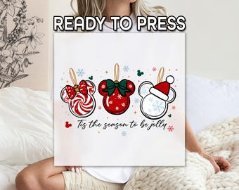 Può includere: Una tela bianca con tre ornamenti natalizi a forma di testa di Topolino. Gli ornamenti sono rossi, bianchi e verdi con disegni festivi. Il testo in basso recita "Tis the season to be jolly". Le parole "READY TO PRESS" sono in alto.