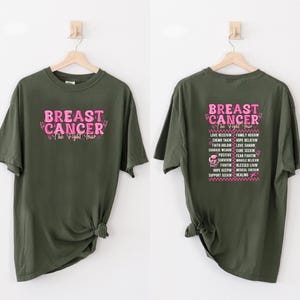 Pu&ograve; includere: Due magliette verde oliva con testo rosa. Una maglietta ha "BREAST CANCER The Fight Tour" sul davanti. L'altra ha lo stesso testo sul retro, insieme a un elenco di parole correlate.