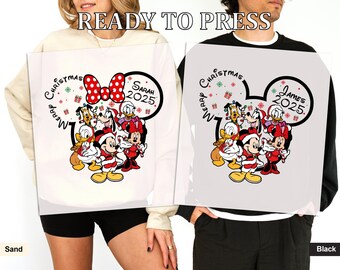 May include: Two sweatshirts, one sand-colored and one black, featuring a Disney Christmas design. The design includes Mickey and Minnie Mouse, Donald Duck, Goofy, and Pluto in Santa outfits. The text "Merry Christmas" and a name and year are also included.
