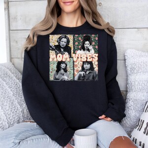 May include: Black sweatshirt with a graphic print of four women with floral backgrounds. The text "MOM VIBES" is printed in white on the graphic.