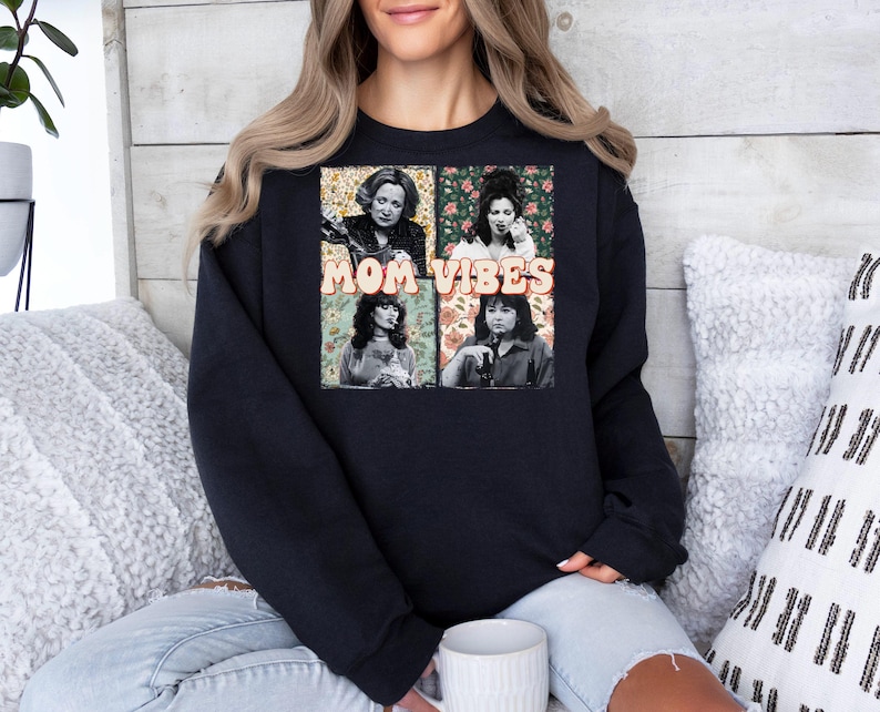 May include: Black sweatshirt with a graphic print of four women with floral backgrounds. The text "MOM VIBES" is printed in white on the graphic.