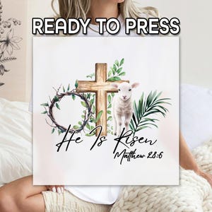 May include: A white t-shirt with a graphic design of a wooden cross, a lamb, and greenery. The text "He Is Risen" and "Matthew 28:6" are printed below the graphic.