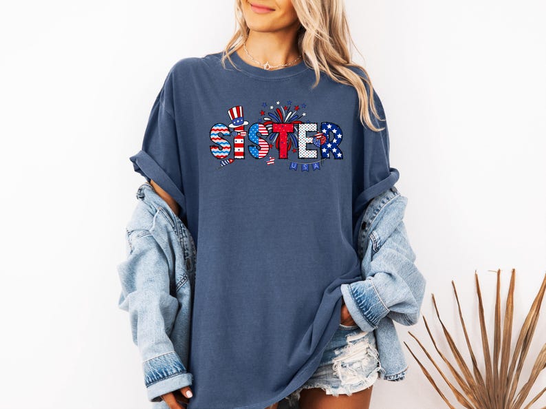 May include: A navy blue t-shirt with a red, white, and blue graphic that says "Sister" with fireworks and a small American flag.