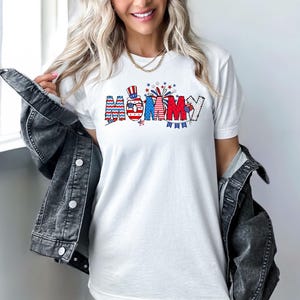 May include: White t-shirt with a red, white, and blue graphic that says "Mommy" with a small American flag and fireworks.