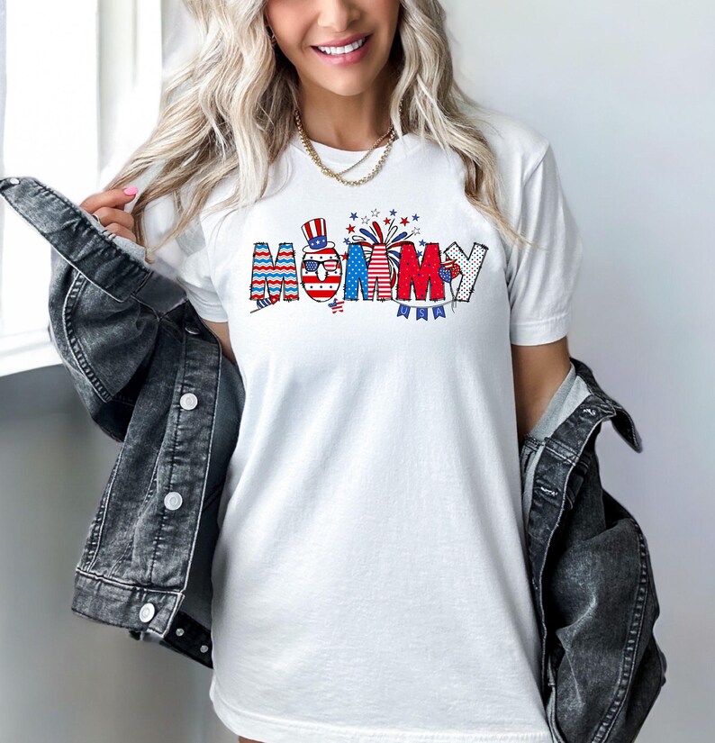 May include: White t-shirt with a red, white, and blue graphic that says "Mommy" with a small American flag and fireworks.