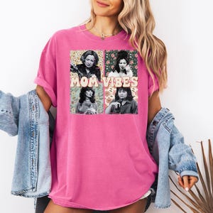 May include: Pink t-shirt with a graphic print of four women with the text "MOM VIBES" in a retro font.
