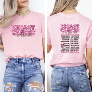 Pu&ograve; includere: Una maglietta rosa chiaro con le parole "BREAST CANCER" in un carattere rosa a fantasia. Il testo "The Fight Tour" &egrave; in basso. Il retro della maglietta presenta un elenco di parole relative alla consapevolezza del cancro al seno.