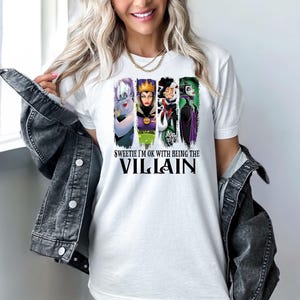Puede incluir: Camiseta blanca con un dise&ntilde;o de cuatro villanos de dibujos animados: &Uacute;rsula, la Reina Malvada, Cruella de Vil y Mal&eacute;fica. El texto de la camiseta dice: "Sweetie I'm OK with Being the Villain".