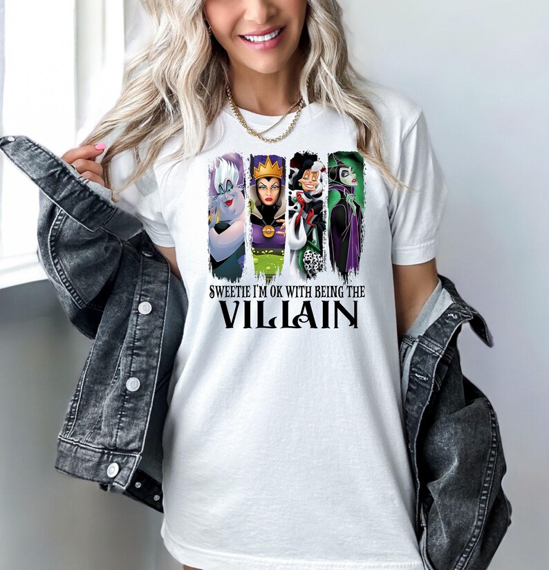 Puede incluir: Camiseta blanca con un dise&ntilde;o de cuatro villanos de dibujos animados: &Uacute;rsula, la Reina Malvada, Cruella de Vil y Mal&eacute;fica. El texto de la camiseta dice: "Sweetie I'm OK with Being the Villain".