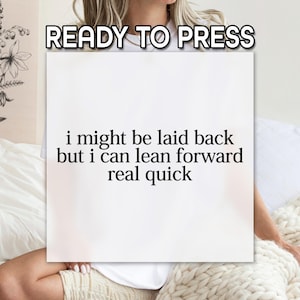 May include: A white square canvas with the text "READY TO PRESS" at the top. The canvas has the quote "i might be laid back but i can lean forward real quick" in a black font. The canvas is held by a person.