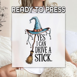May include: A white square with a witch hat and broom illustration. The hat is blue with a brown band and buckle. The broom is brown and gold. Text reads "YES I CAN DRIVE A STICK."