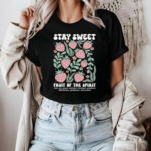 May include: Black t-shirt with the text "STAY SWEET" above a graphic of strawberries and leaves. Below the graphic, the text "FRUIT OF THE SPIRIT" is displayed, followed by a list of virtues.