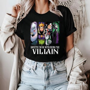 Puede incluir: Camiseta negra con un dise&ntilde;o de cuatro villanos de dibujos animados: &Uacute;rsula, la Reina Malvada, Cruella de Vil y Mal&eacute;fica. El texto "Sweetie I'm OK with Being the Villain" est&aacute; impreso en blanco.