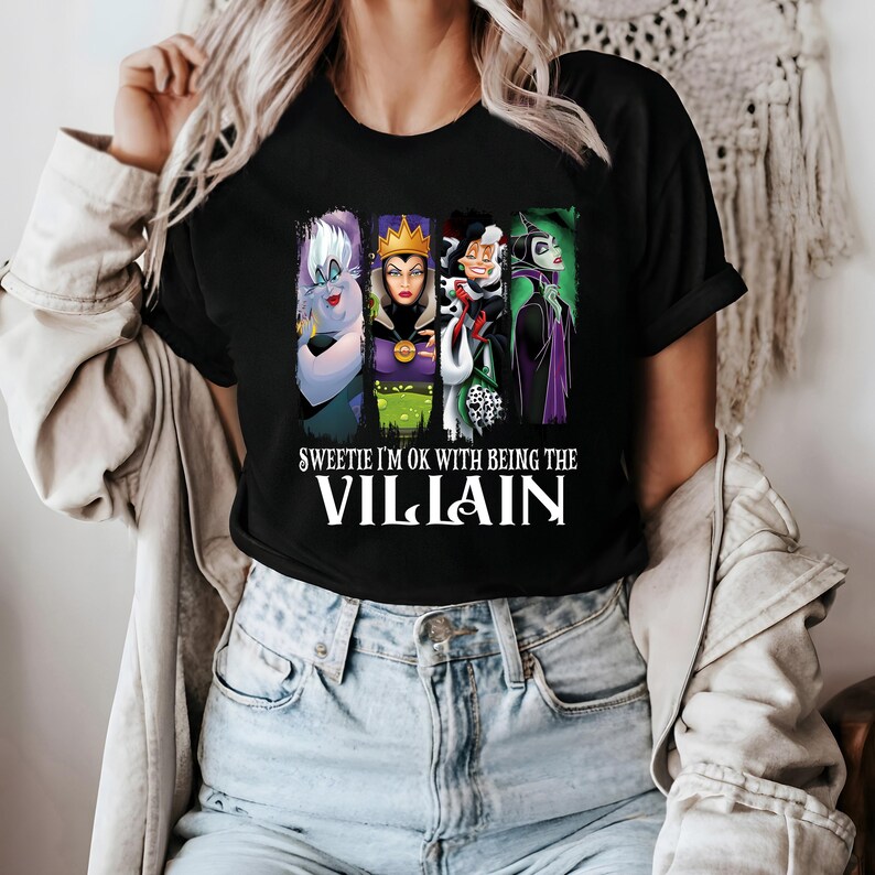 Puede incluir: Camiseta negra con un dise&ntilde;o de cuatro villanos de dibujos animados: &Uacute;rsula, la Reina Malvada, Cruella de Vil y Mal&eacute;fica. El texto "Sweetie I'm OK with Being the Villain" est&aacute; impreso en blanco.