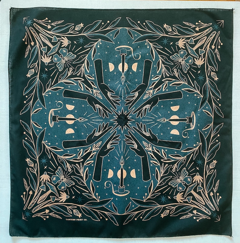 May include: A green bandana with a white and gold design featuring a repeating pattern of hands, candles, and moons. The bandana has the text "LANTERN PREST CO." at the bottom.