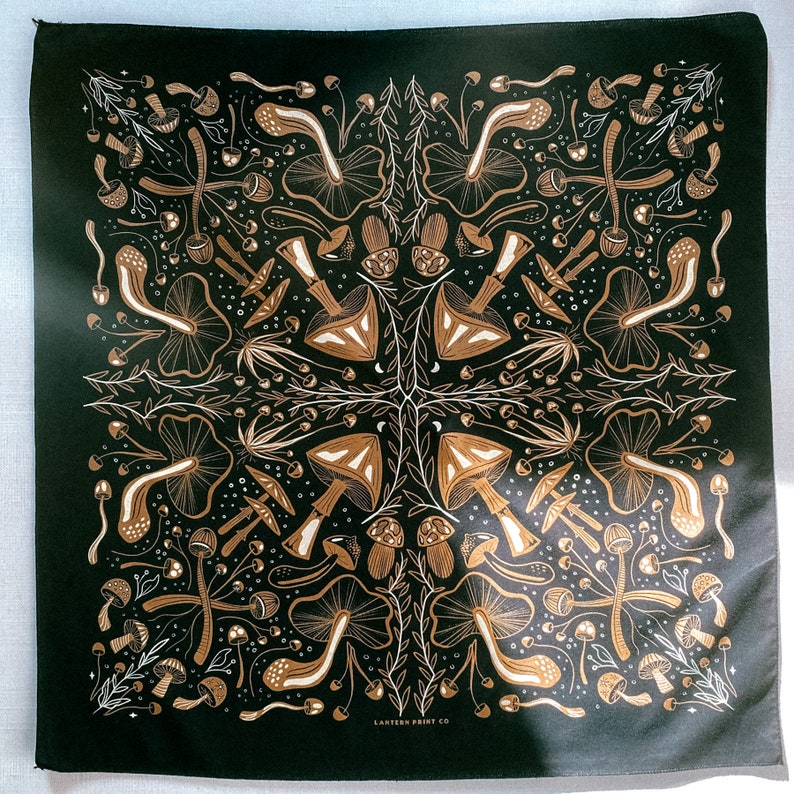 Op de afbeelding: Een zwarte bandana met een wit ontwerp van paddenstoelen en bladeren. De bandana heeft de tekst "LANTERN PRINT CO."