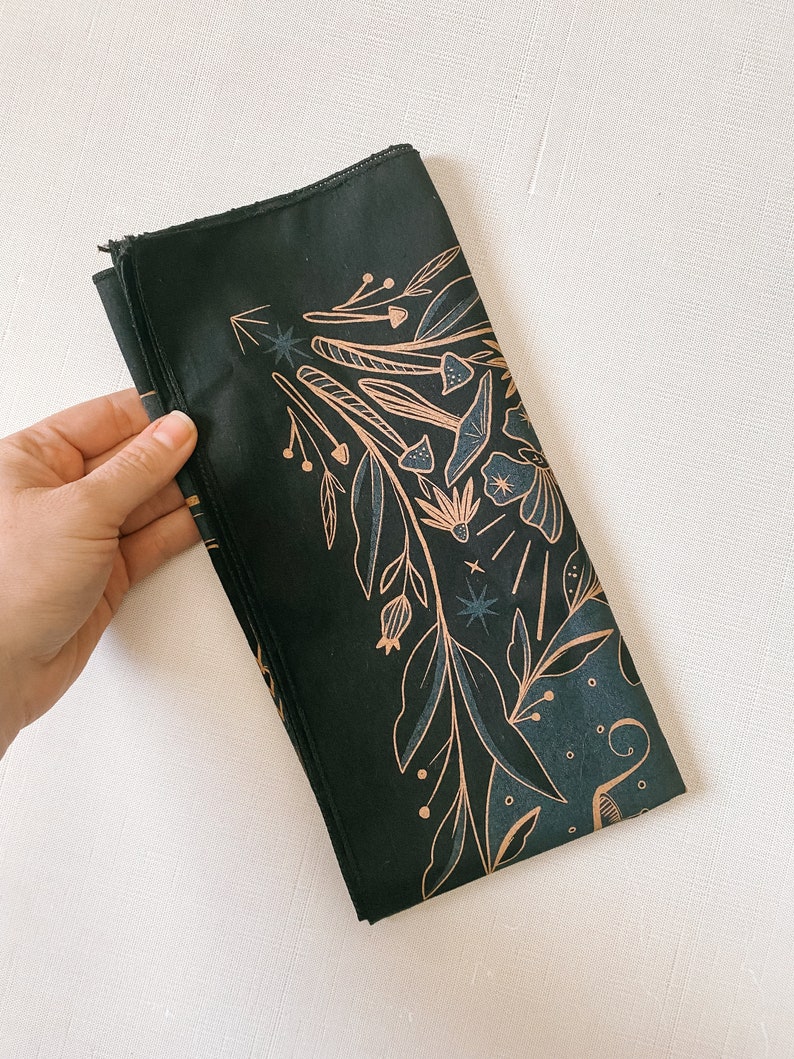 May include: A black bandana with a gold floral design. The design features leaves, flowers, and mushrooms.