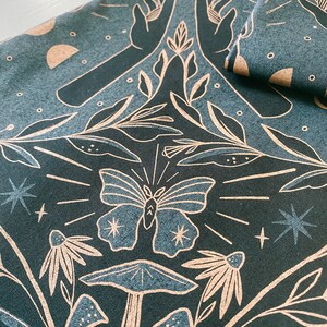 May include: A dark blue fabric with a white design of hands reaching up towards a butterfly, mushrooms, and stars. The design is reminiscent of a forest scene.