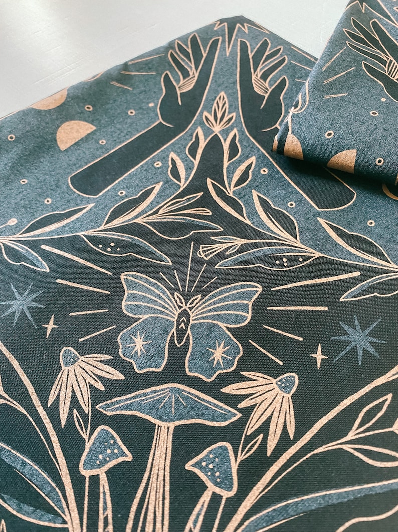 May include: A dark blue fabric with a white design of hands reaching up towards a butterfly, mushrooms, and stars. The design is reminiscent of a forest scene.