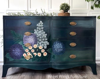 May include: A dark teal dresser with six drawers and gold-toned hardware. The front of the dresser is decorated with floral artwork featuring purple hydrangeas, white and yellow roses, and blue flowers. The text "Angel Wings Furniture" is visible at the bottom.