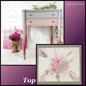 May include: A two-drawer side table with a gray and pink ombre paint finish. The table has gold hardware and gold painted legs. The top of the table is painted with a pink and gray abstract design.