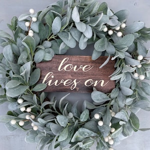 May include: A green and white wreath with a wooden sign that reads "love lives on".
