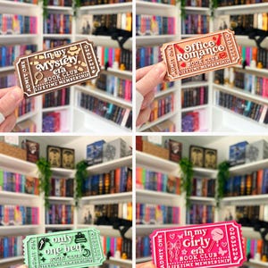 May include: A collection of four rectangular plastic ticket-shaped ornaments featuring book club themes. The brown ticket reads In my Mystery era, the peach ticket reads Office Romance, the mint ticket reads only one bed, and the pink ticket reads In my Girly era.