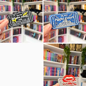May include: A collection of three rectangular ticket-shaped bookmarks featuring book club themes. One is black with yellow dragon graphics, one is blue with white mountain and bat motifs, and one is white with a red pair of vampire fangs and blood drops.