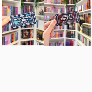 May include: Two rectangular stickers shaped like admission tickets. One is dark blue with white text reading The never-ending TBR BOOK CLUB LIFETIME MEMBERSHIP. The other is dark blue with white and red text reading SPORTS ROMANCE BOOK CLUB.