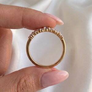 May include: A gold band ring featuring a row of small, clear, round-cut stones set along the top half of the circular metal frame. The ring has a polished finish and a smooth, solid gold shank that completes the circular design of the jewelry piece.