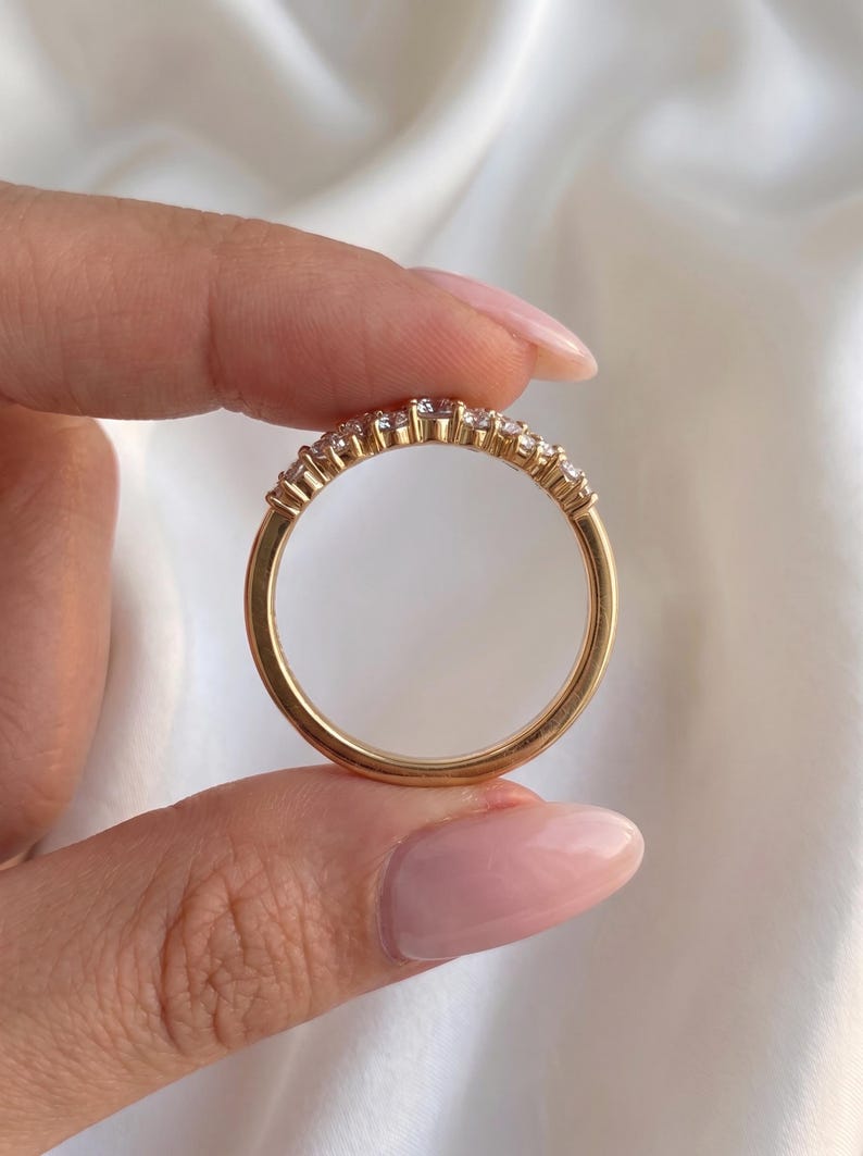 May include: A gold band ring featuring a row of small, clear, round-cut stones set along the top half of the circular metal frame. The ring has a polished finish and a smooth, solid gold shank that completes the circular design of the jewelry piece.