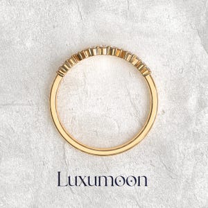 May include: A gold ring featuring a curved row of small, clear, round-cut stones set along the top half of the band. The band is smooth and polished, with the brand name Luxumoon printed in dark blue text below the jewelry piece.