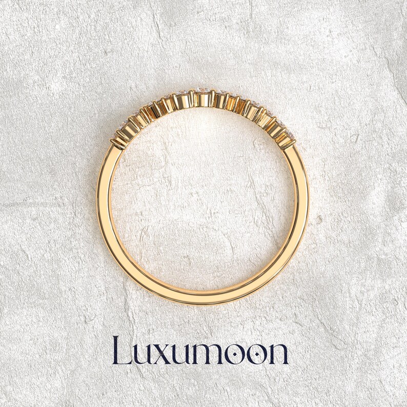 May include: A gold ring featuring a curved row of small, clear, round-cut stones set along the top half of the band. The band is smooth and polished, with the brand name Luxumoon printed in dark blue text below the jewelry piece.
