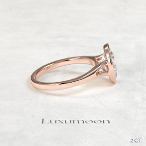 May include: A rose gold ring featuring a clear, pear-shaped gemstone set in a bezel setting. The band is smooth and polished. The text Luxumoon is printed below the ring, with the text 2 CT positioned in the bottom right corner of the image.