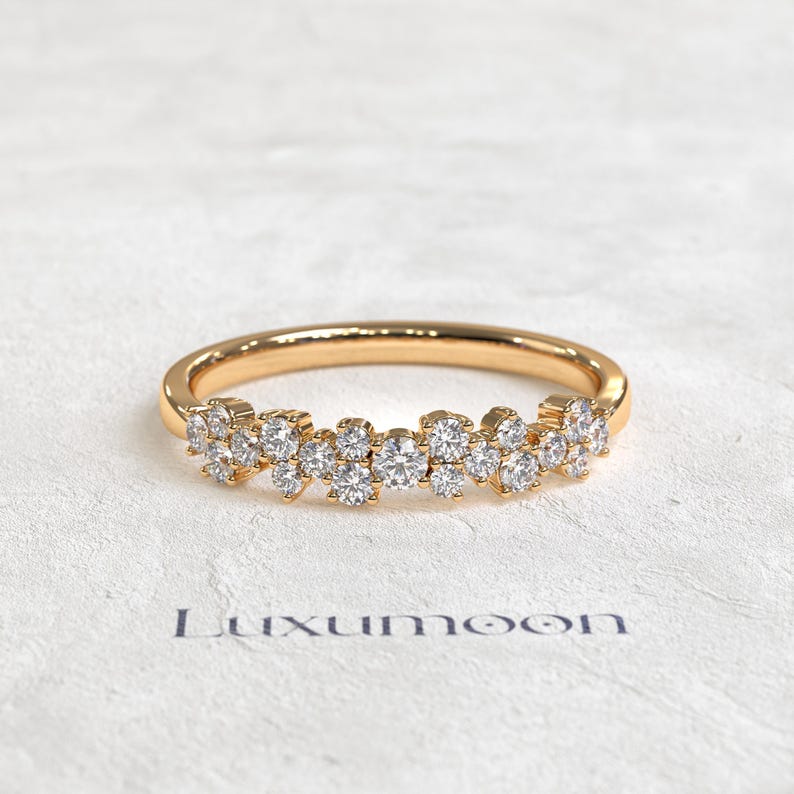 May include: A gold ring featuring a cluster of small, round, clear stones set along the front half of the band. The band has a polished finish and the stones are arranged in a dense, multi-layered formation. The text Luxumoon is printed below.