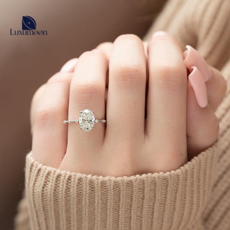 May include: A silver engagement ring featuring an oval-shaped diamond set in a delicate, beaded band.