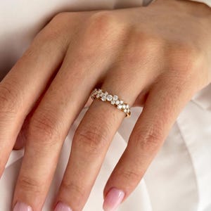 May include: A gold band ring featuring a cluster of multiple small, round, clear, faceted stones arranged in a staggered, multi-layered pattern across the top surface of the band, creating a textured, sparkling appearance on the finger.