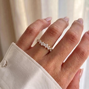 May include: A gold band ring featuring a cluster of small, round, clear, faceted stones set in a continuous row around the circumference. The ring is worn on a finger, showcasing the sparkling stones against the polished yellow gold metal setting.