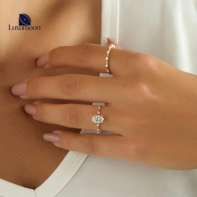 May include: A gold ring featuring a large oval-shaped diamond surrounded by smaller diamonds. The ring is worn on a person's finger.