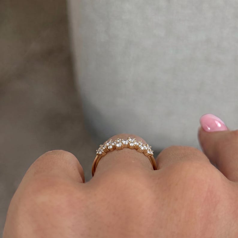 May include: A gold ring featuring a curved band set with a row of small, clear, round-cut stones. The band has a polished metallic finish and the stones are arranged in a cluster formation along the top arc of the ring, creating a sparkling effect.