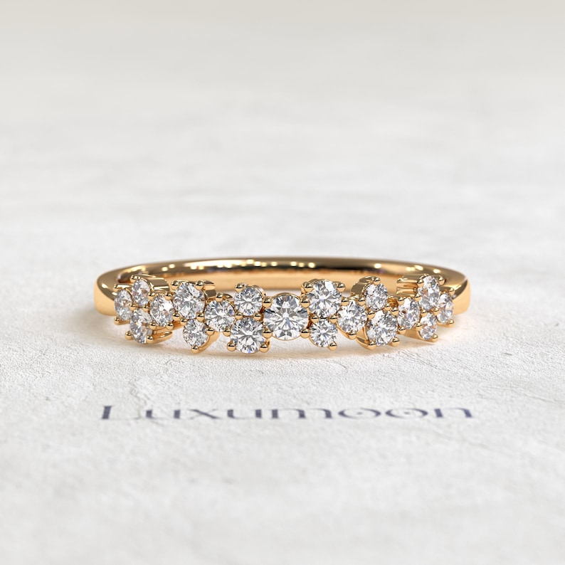 May include: A gold ring featuring a cluster of round brilliant-cut clear stones arranged in a horizontal row across the top of the band. The stones vary slightly in size, creating a textured, sparkling surface. The word Luxumoon is printed below.