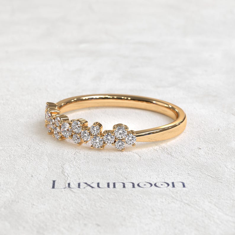 May include: A gold ring featuring a cluster of small, round, clear stones set along the top half of the band. The band has a smooth, polished finish. The word Luxumoon is printed in dark letters below the ring on the textured surface.