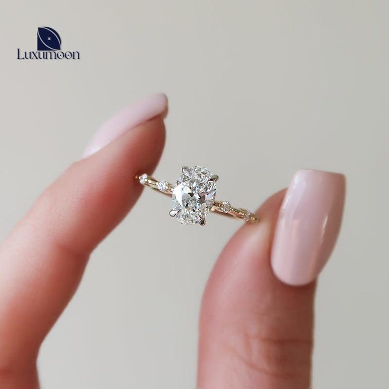 May include: A delicate gold engagement ring featuring a large oval-shaped diamond set in a prong setting. The band is adorned with smaller diamonds that create a delicate vine-like design.