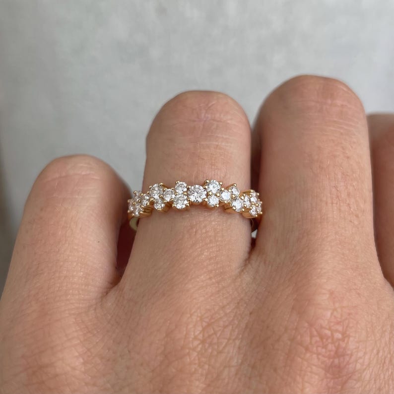 May include: A gold band ring featuring a cluster of small, round, clear, faceted stones arranged in a staggered, multi-level row across the top. The stones are set in a polished gold metal setting that follows the contour of the stones.