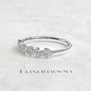 May include: A silver-toned ring featuring a cluster of small, round, clear stones set along the top half of the band. The band is smooth and polished. The word Luxumoon is printed in dark letters below the ring on the textured surface.